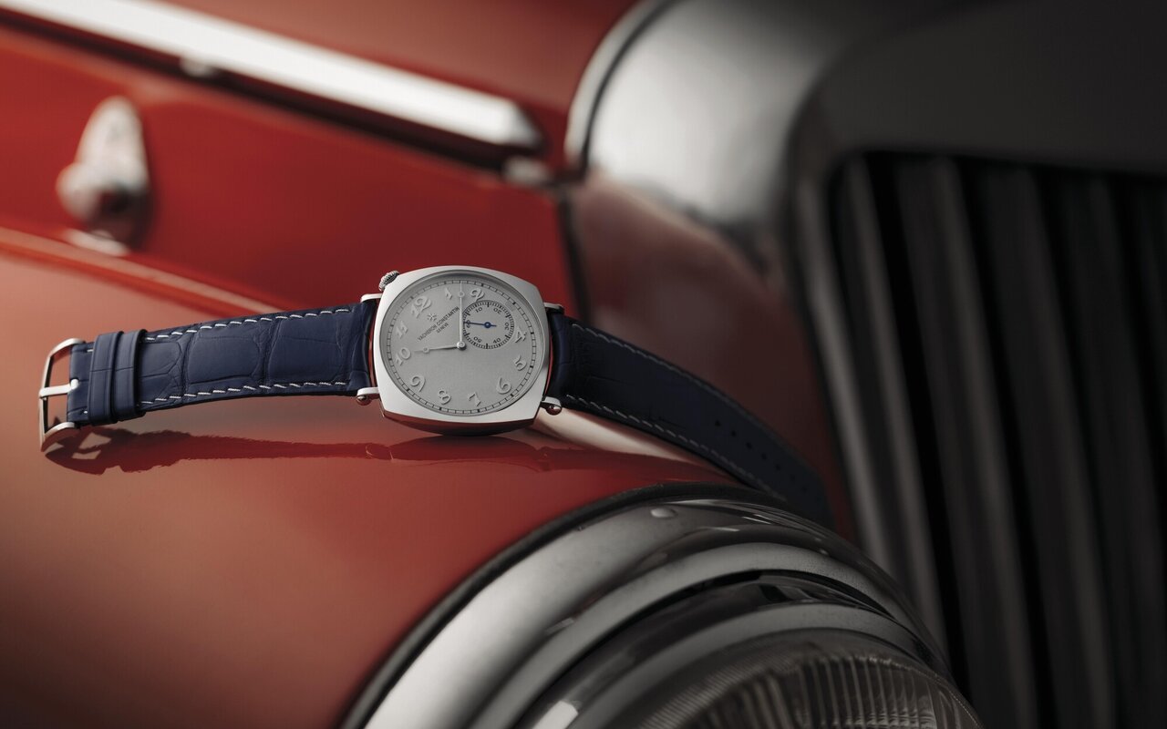 Montre Vacheron Constantin Historiques American 1921, boîtier coussin, cadran argenté incliné et bracelet alligator bleu nuit, posée sur la carrosserie rouge d'une voiture ancienne