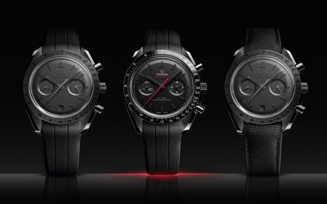 Trois chronographes Omega Speedmaster en céramique noire alignés sur fond noir, celui du centre avec une aiguille rouge